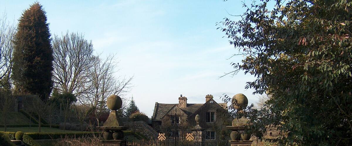 A gated entrance to a historic building with stone walls and a gravel path leading to it.