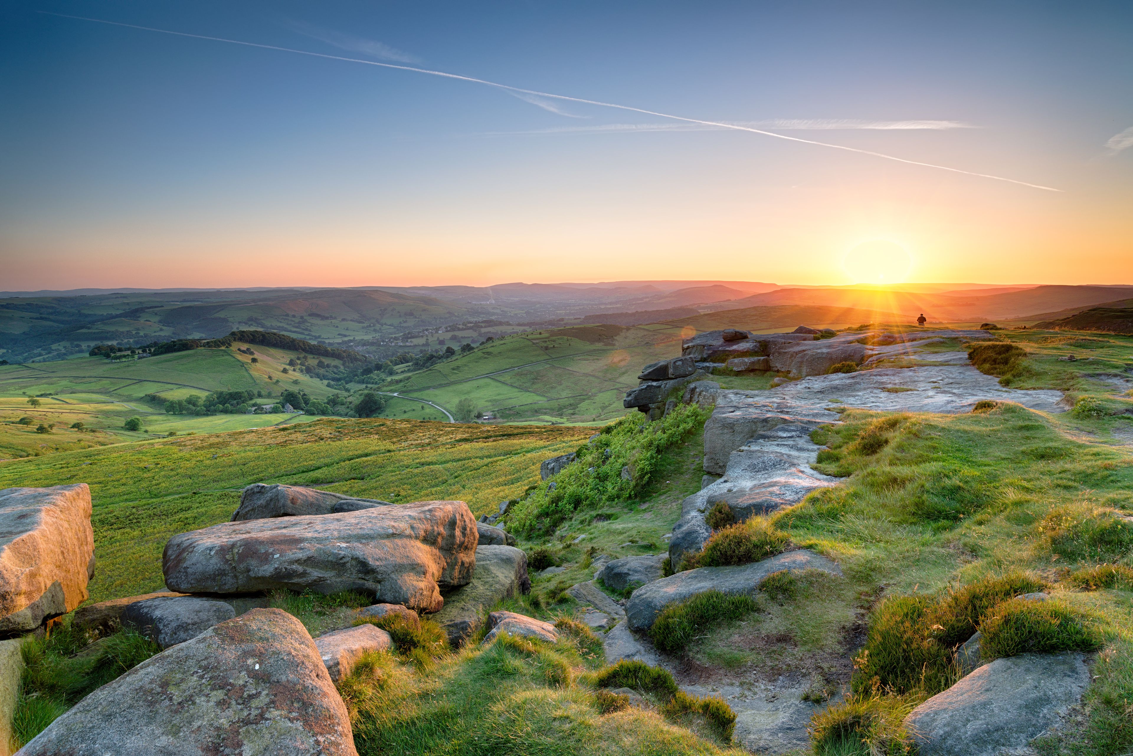 A landscape with rolling hills, a winding path, and a sunset in the distance.