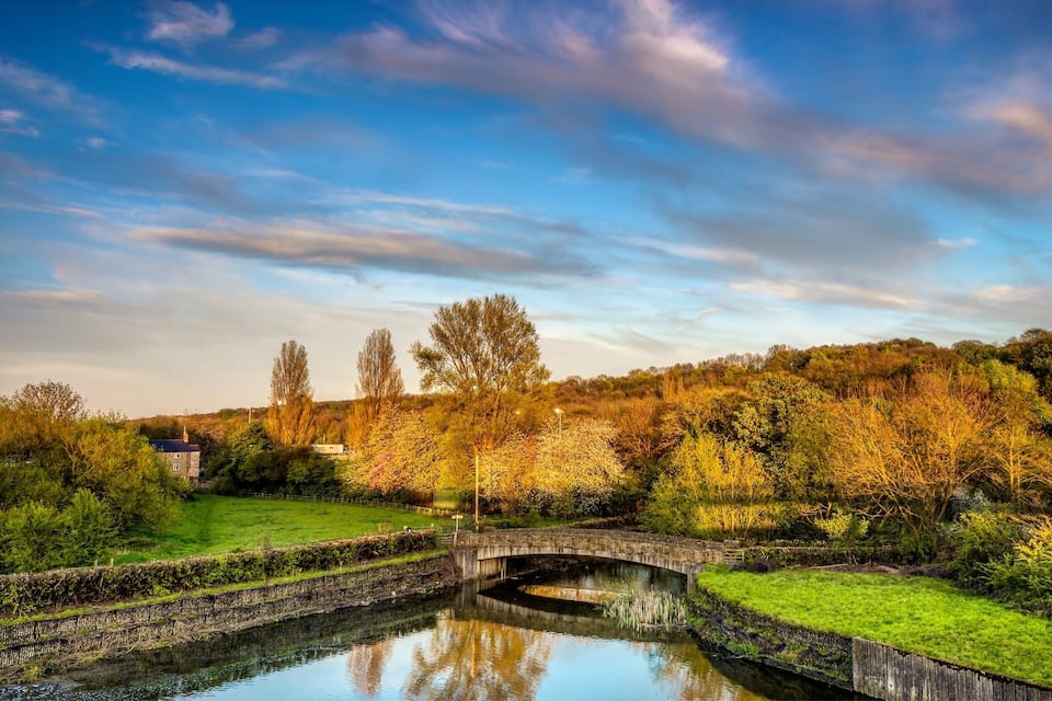 A stone bridge over a calm river, surrounded by lush greenery and trees.