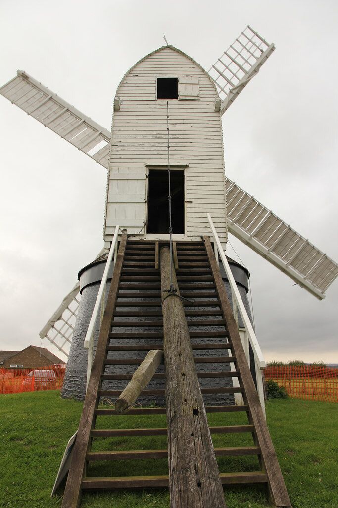 A white windmill with a wooden staircase leading up to its entrance.