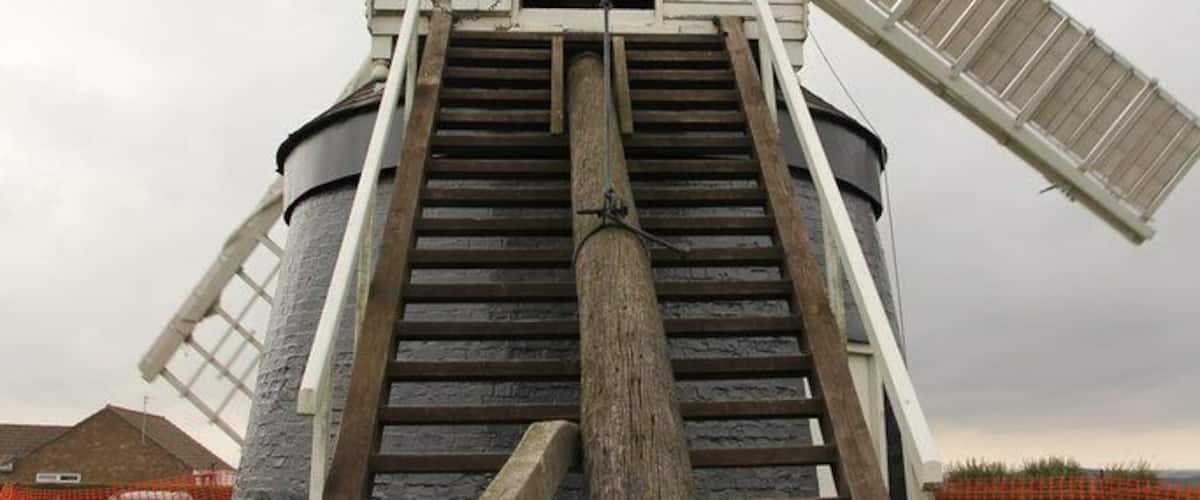 A white windmill with a wooden staircase leading up to its entrance.