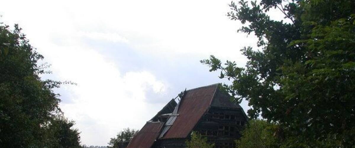 A tilted barn in a rural setting with a path leading to it.