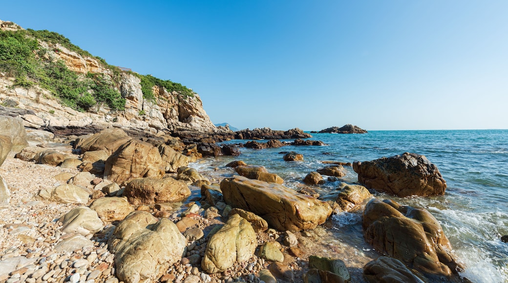Una costa rocciosa con grandi massi e un cielo azzurro limpido.