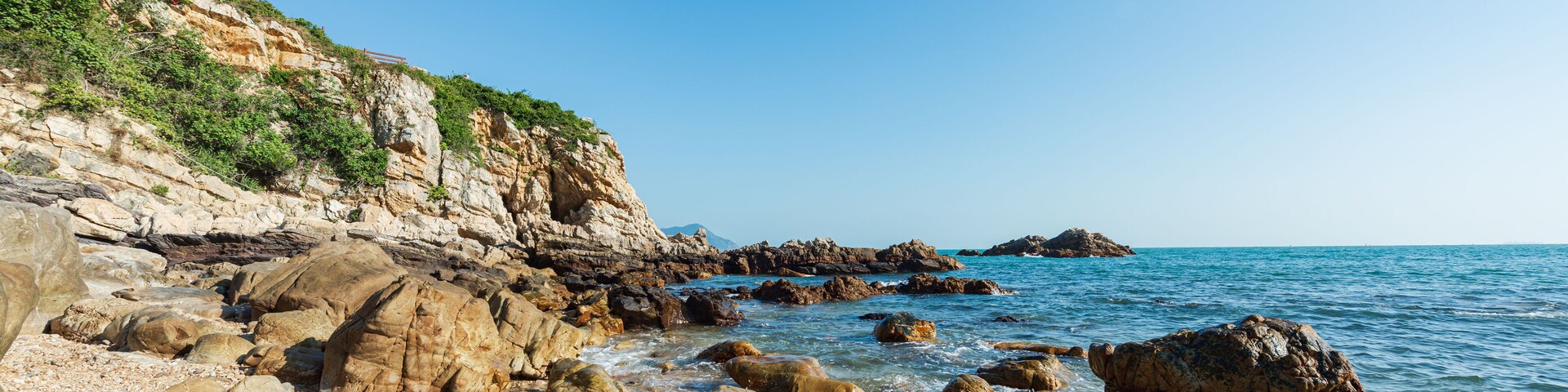 Linha de costa rochosa com grandes pedras e céu azul límpido.