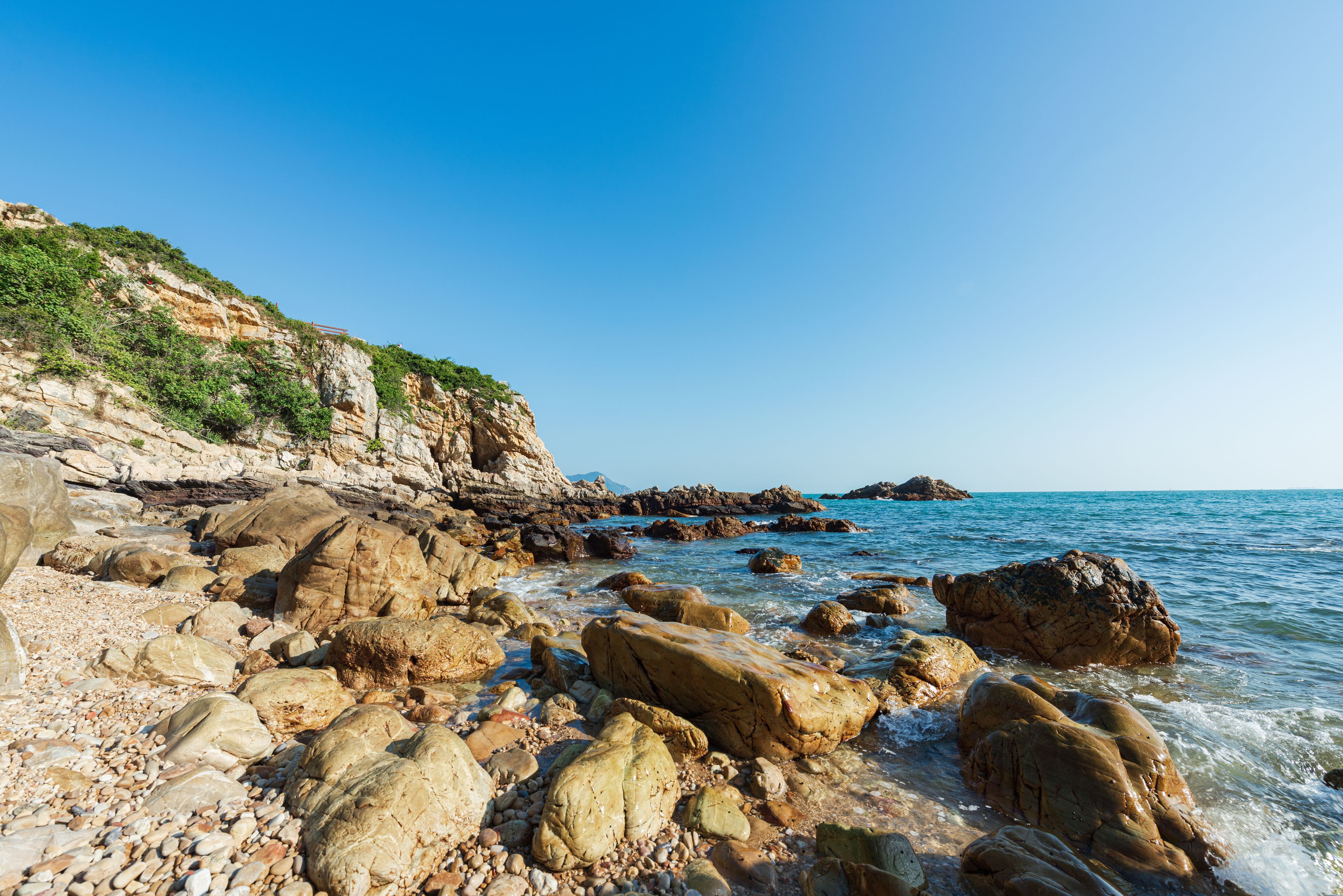 A rocky shoreline with large boulders and a clear blue sky.