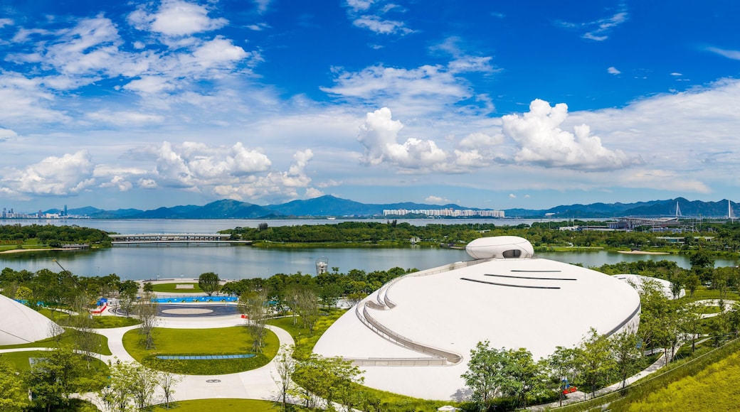 A modern architectural complex with unique white structures, a lake, and a city skyline in the background.