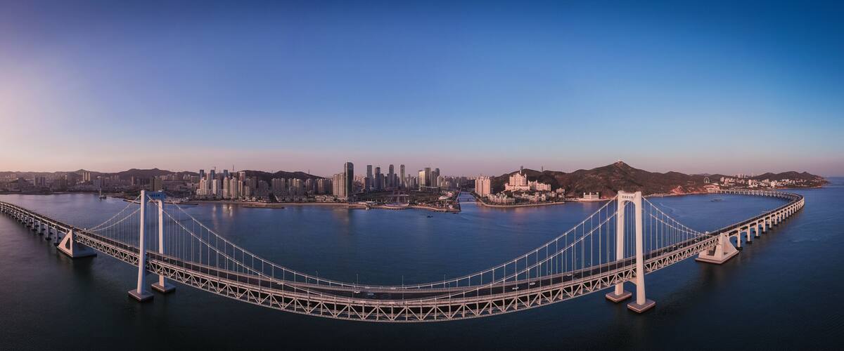 A large suspension bridge spanning a wide body of water with a cityscape in the background.