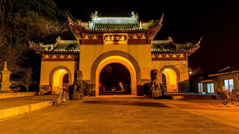 A traditional Chinese gate at night with intricate architecture and a bicycle parked nearby.