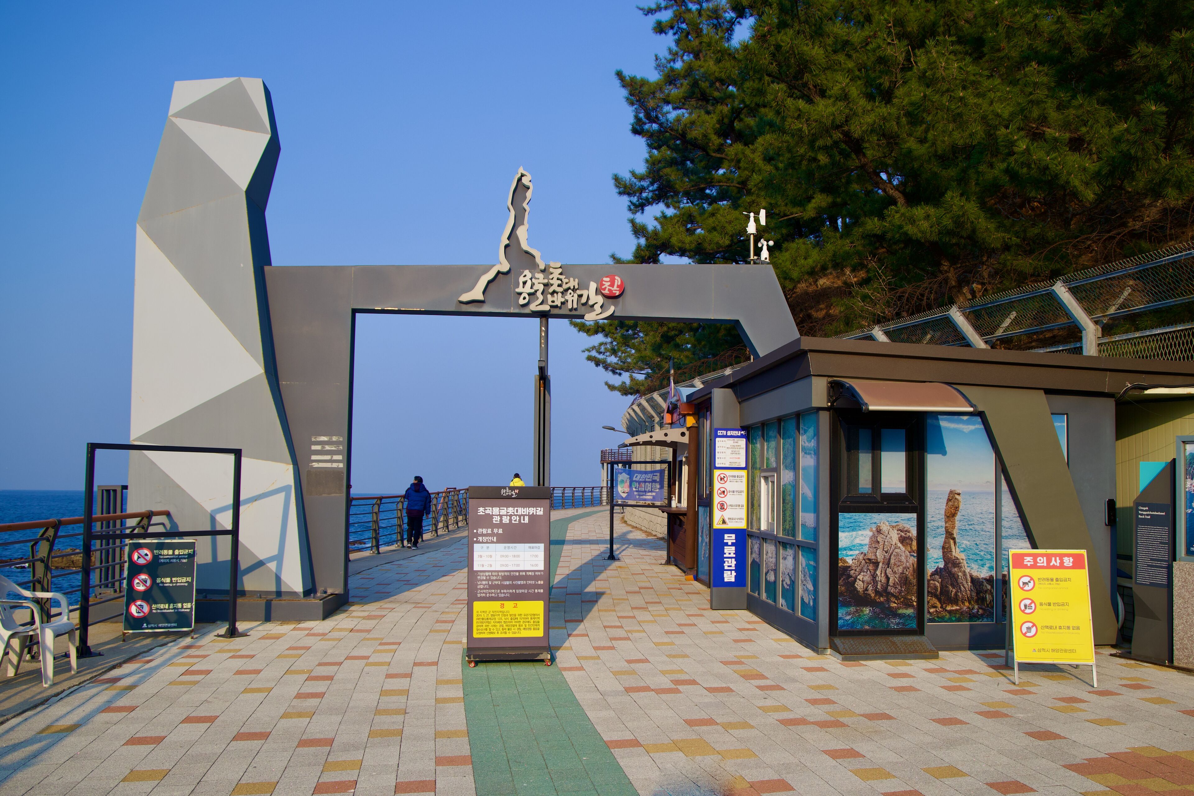 A coastal walkway with a large archway, informational signs, and a view of the sea.