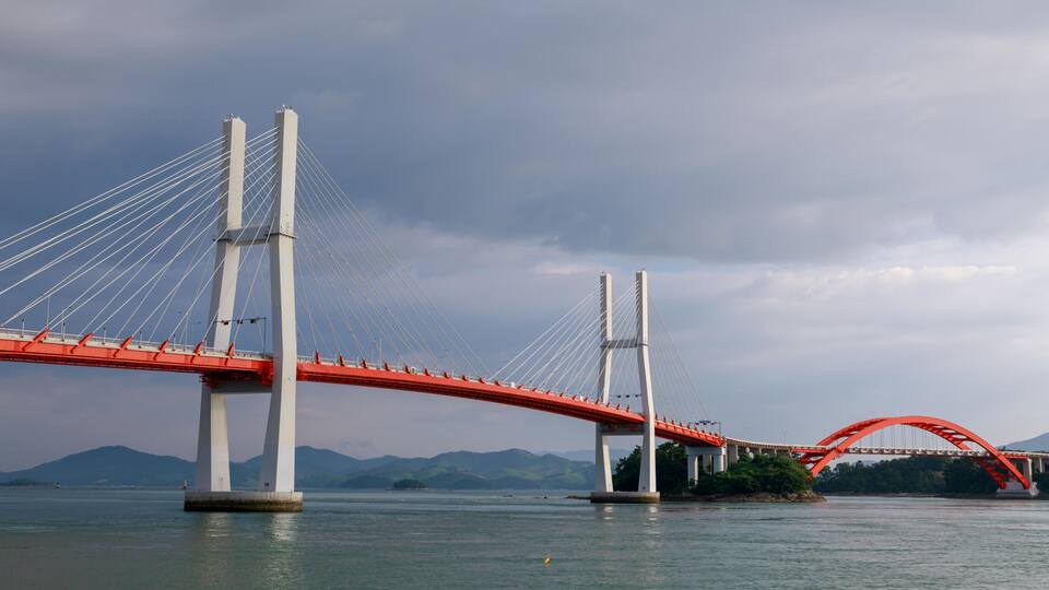 A red suspension bridge over a body of water with mountains in the background.