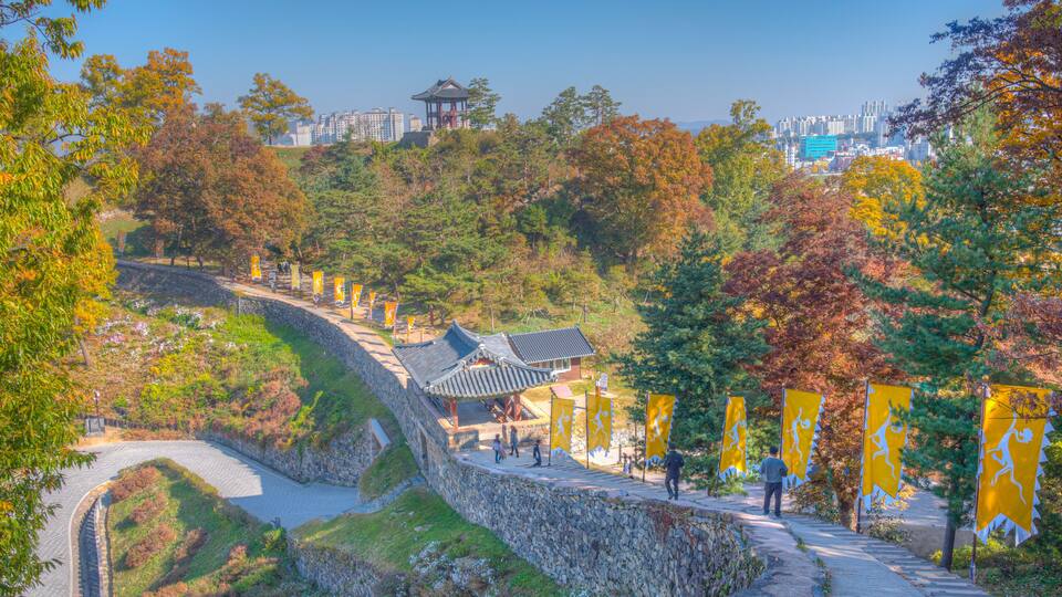 A traditional Korean pavilion, stone walls, and a pathway with yellow flags.