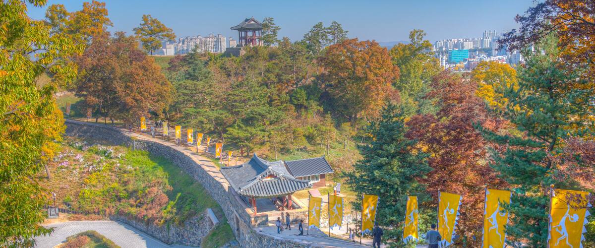 A traditional Korean pavilion, stone walls, and a pathway with yellow flags.