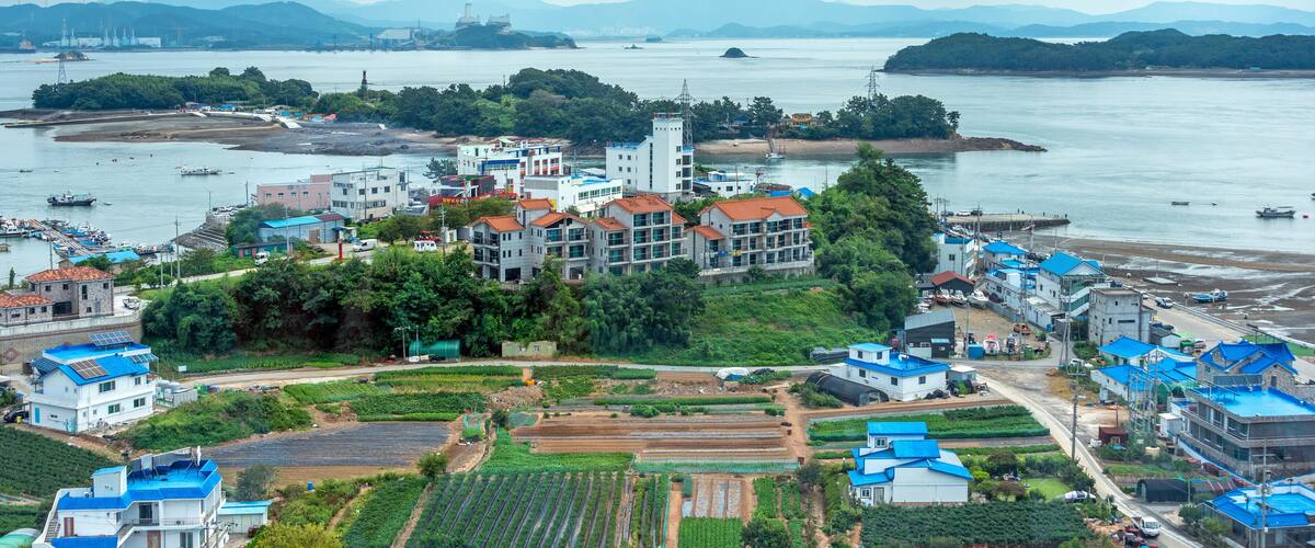 A coastal town with residential buildings, a harbor, and agricultural fields.