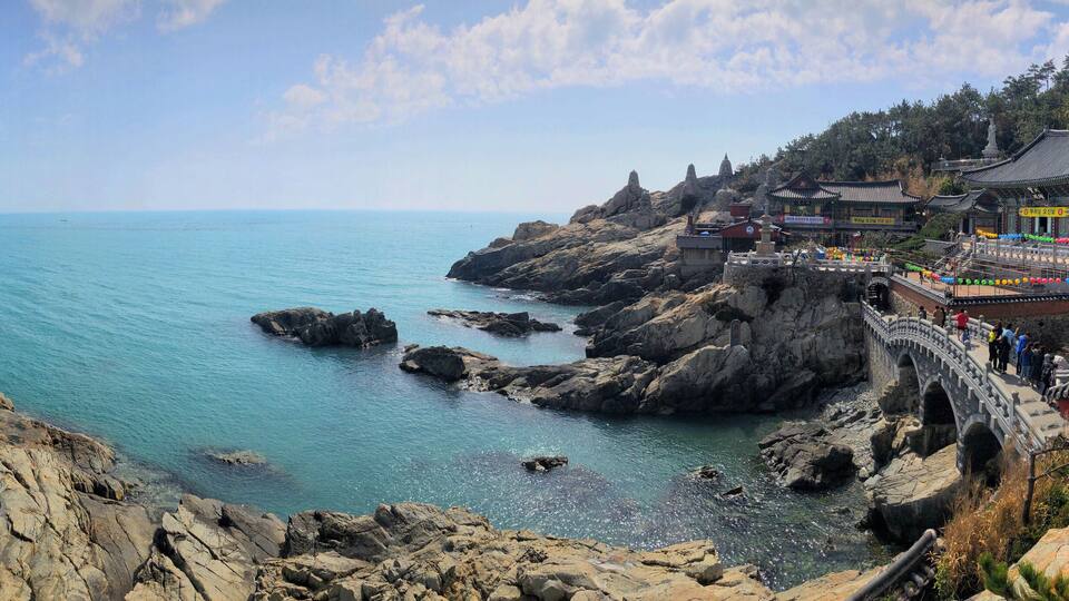 A coastal landscape with rocky cliffs, a clear blue sea, and traditional architecture.