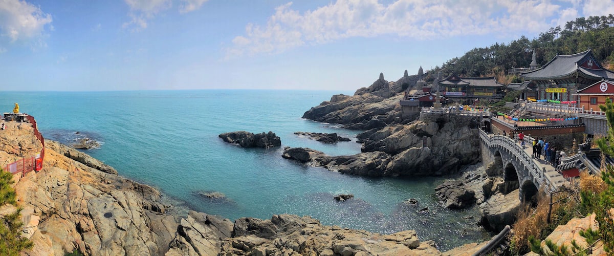 A coastal landscape with rocky cliffs, a clear blue sea, and traditional architecture.
