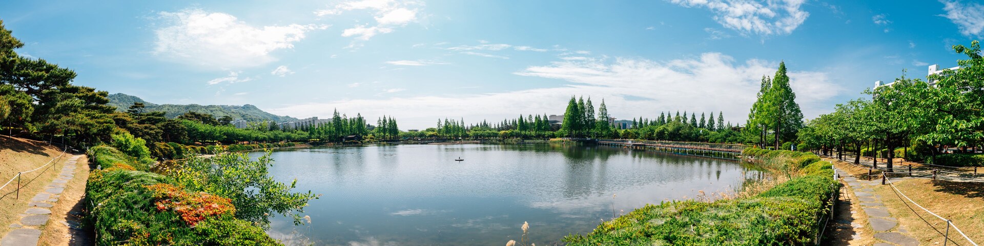 Un lago tranquilo rodeado de abundante vegetación y árboles, con un sendero de piedra a la orilla.