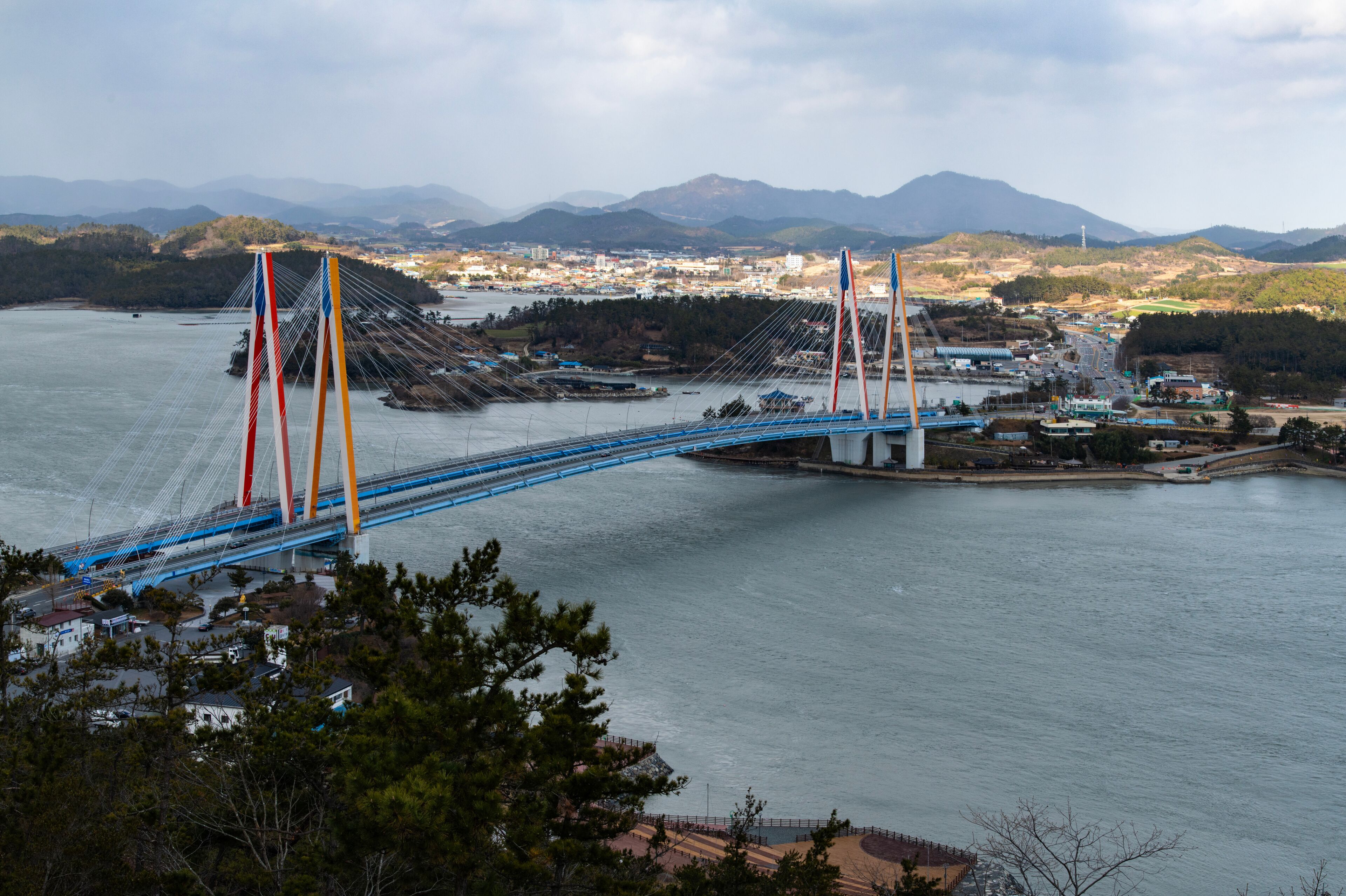 A cable-stayed bridge spanning a river with mountains in the background.