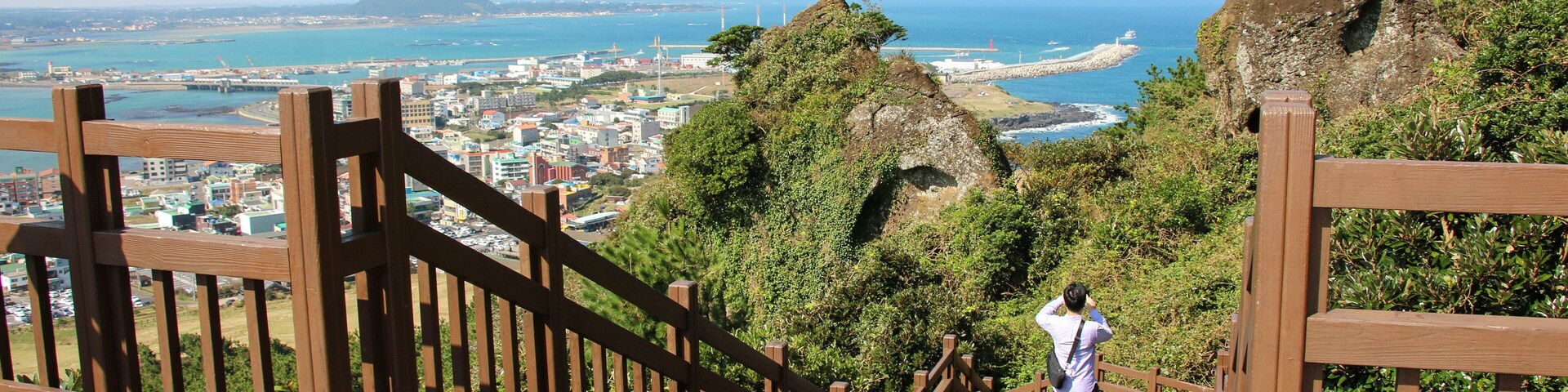Una escalera de madera que conduce a un mirador con vistas a una ciudad costera y una montaña al fondo.