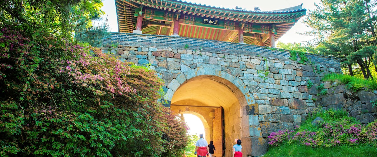 A traditional Korean gate with a stone archway, surrounded by lush greenery and flowering plants.