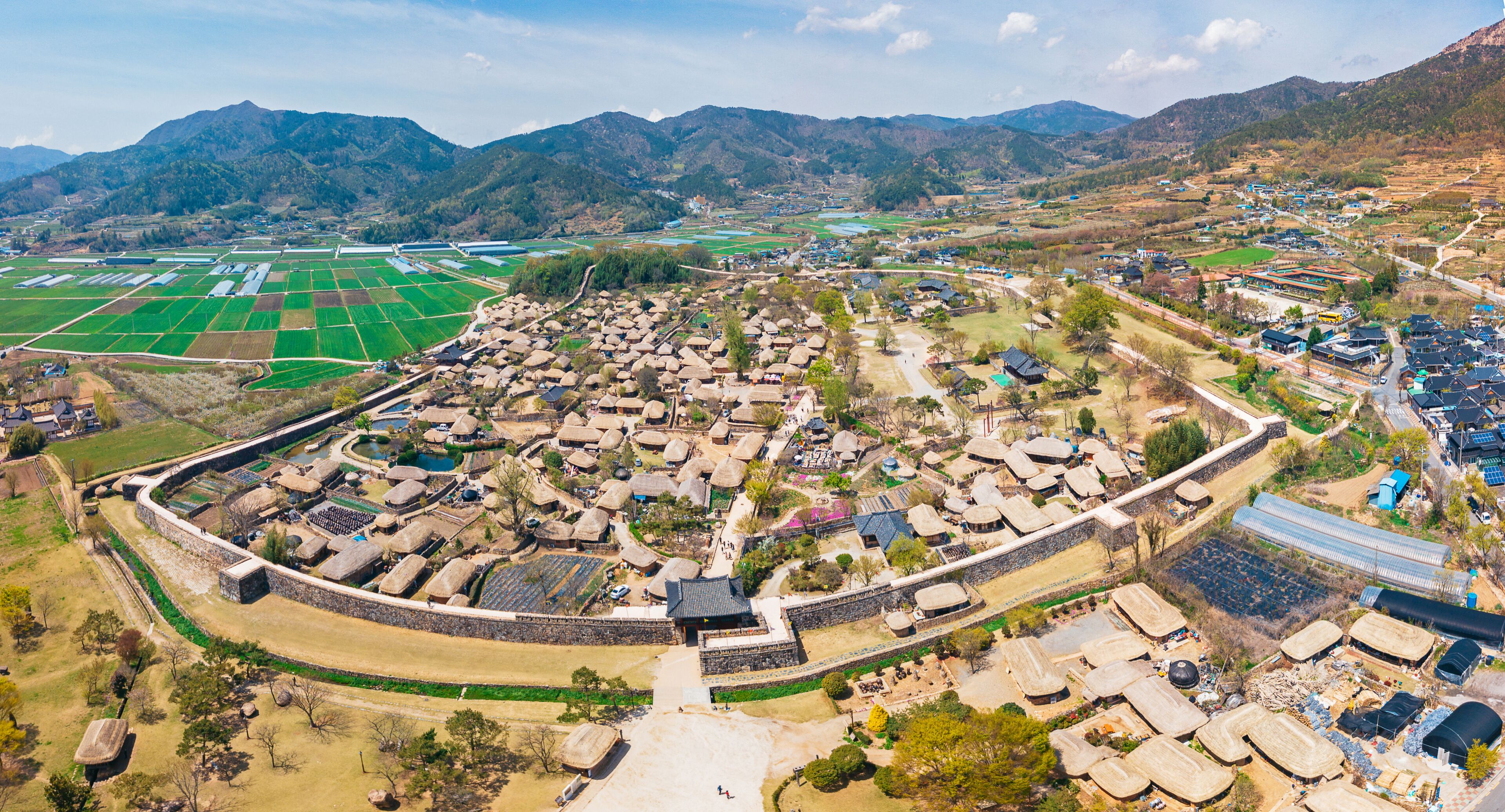 An aerial view of a village with traditional houses, surrounded by fields and mountains.