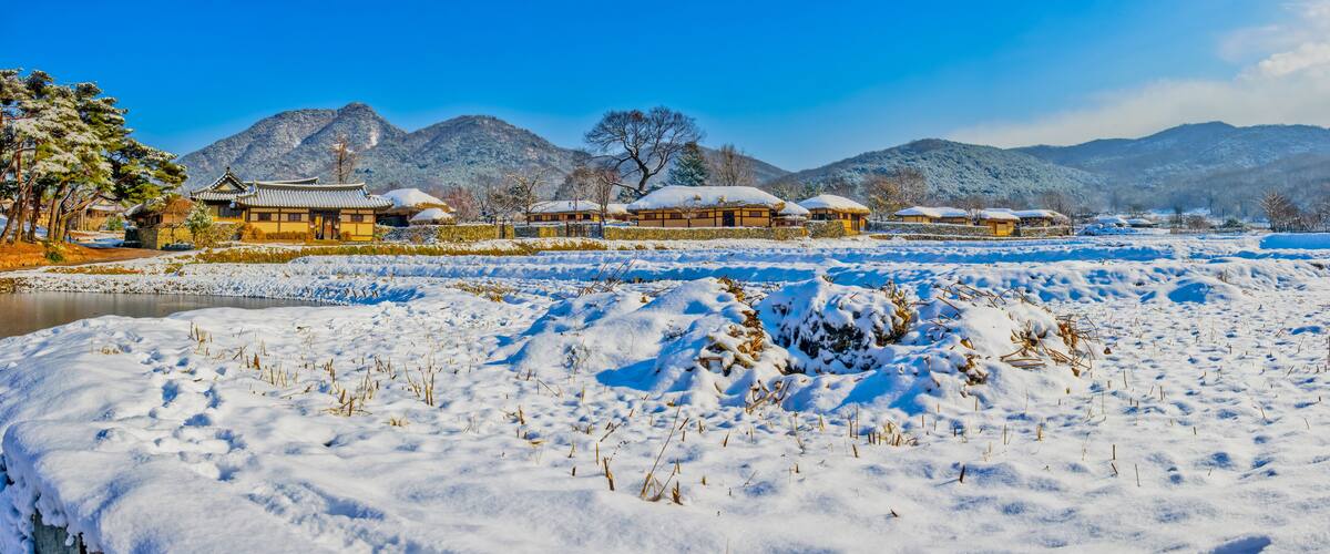 A snow-covered landscape with traditional buildings and mountains in the background.