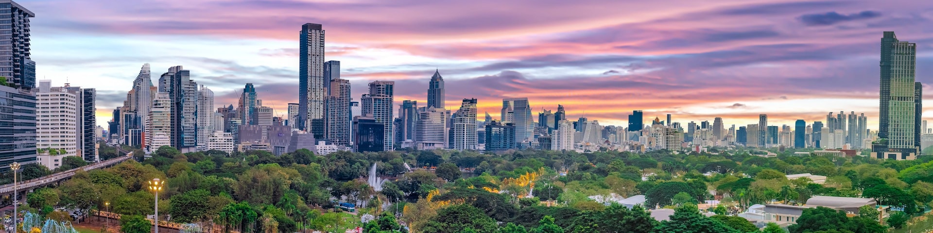 Horizonte urbano com arranha-céus modernos e um parque com árvores e uma estátua.