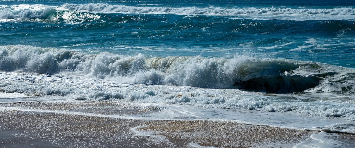A beach with waves crashing onto the shore under a clear blue sky.