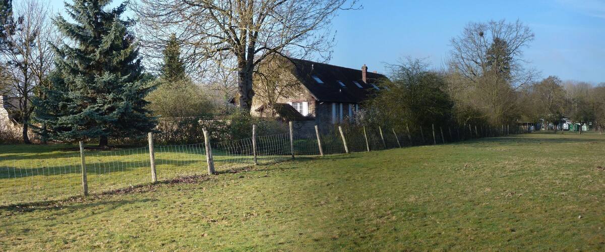 A rural landscape with a house, a fenced field, and a forest in the background.