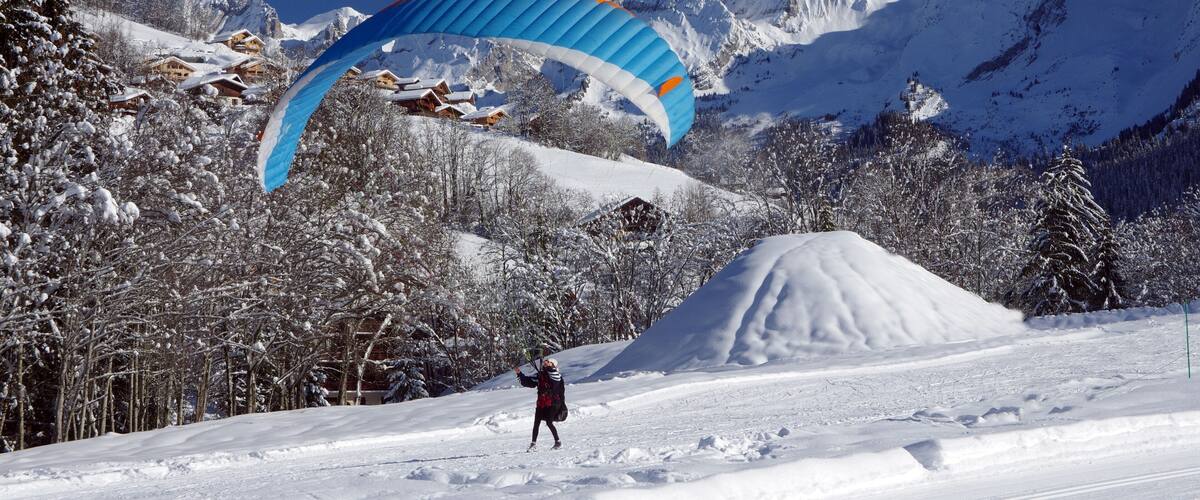 A person paragliding over a snowy mountain landscape with snow-covered trees and houses.