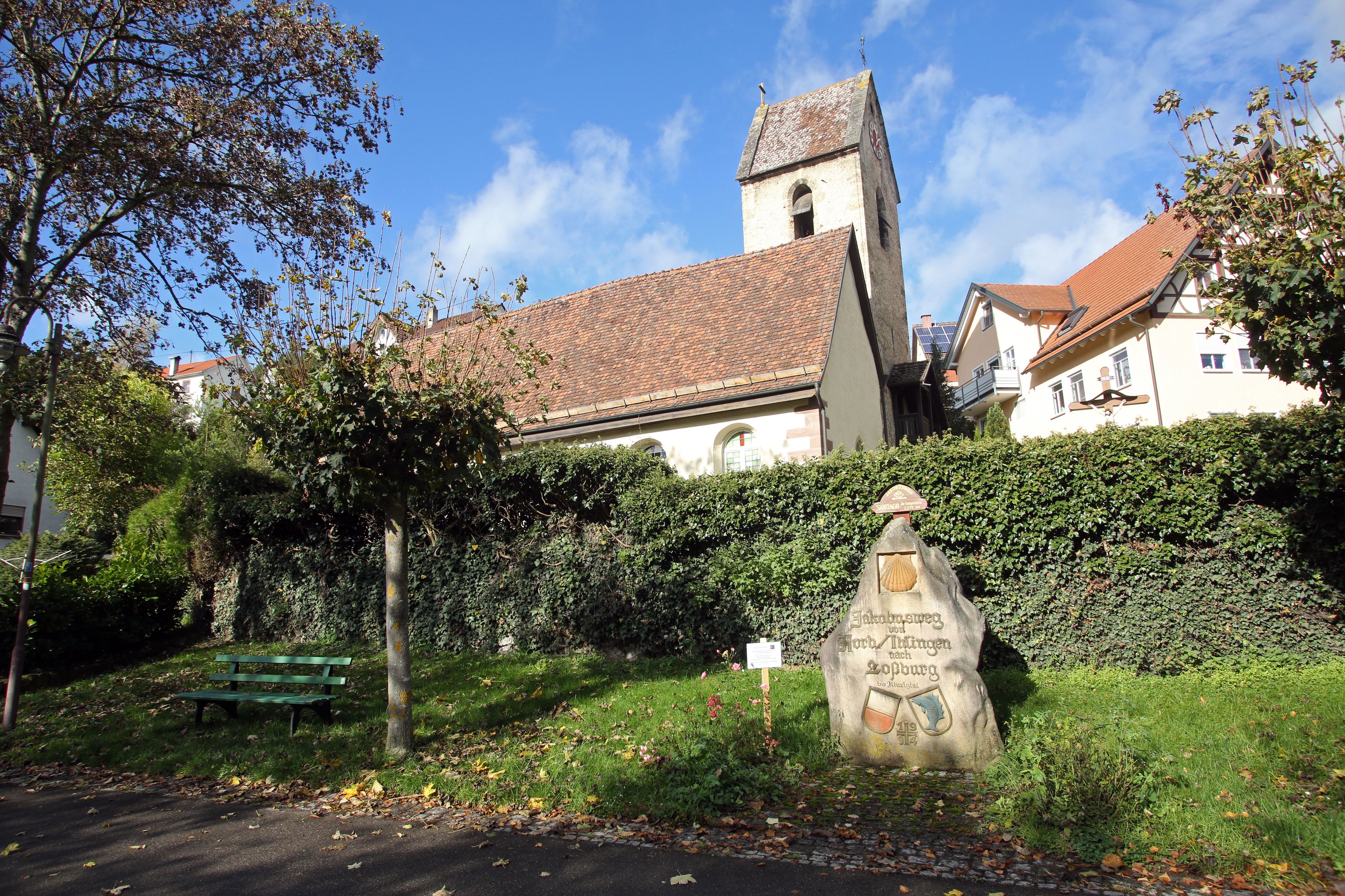 A church with a bell tower, a stone monument, and a bench in a park.