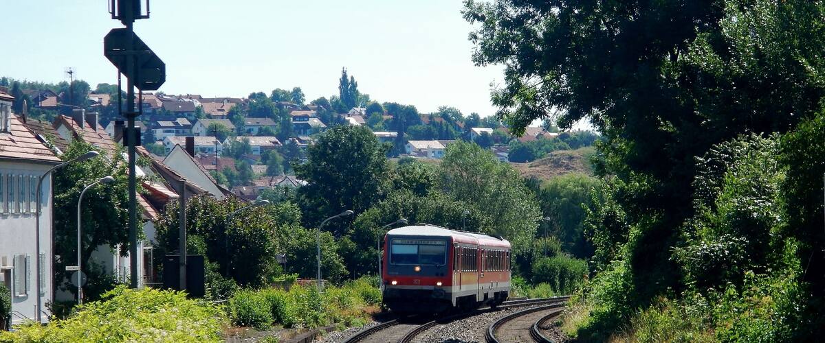 A train on a curved track with houses and greenery in the background.