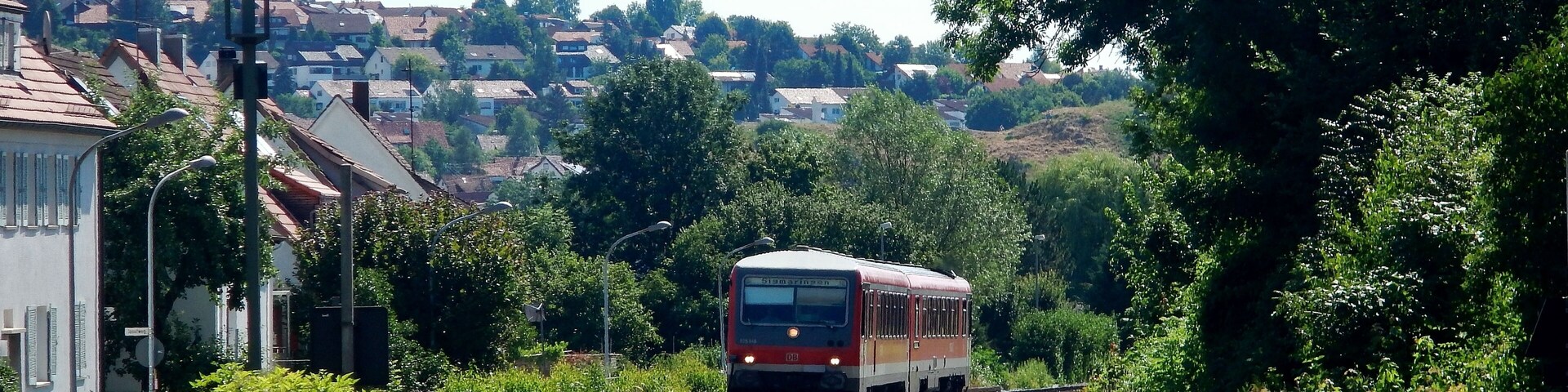 A train on a curved track with houses and greenery in the background.
