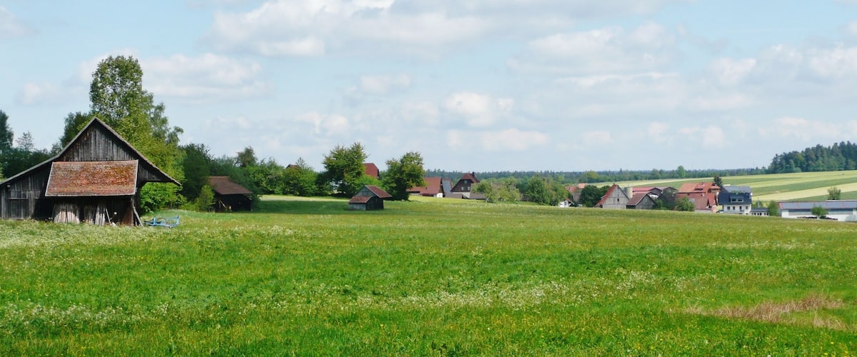 A rural landscape with a barn, several houses, and a field.