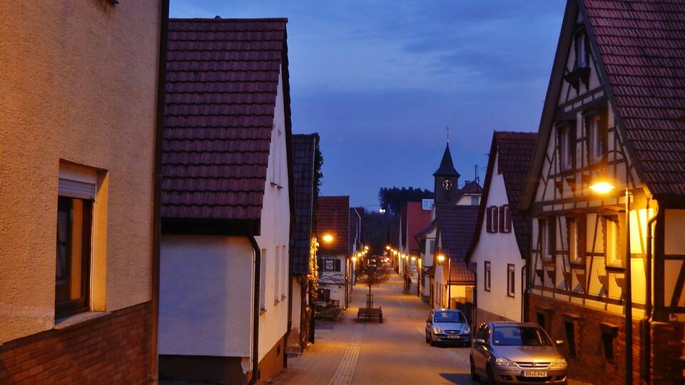 A narrow street lined with traditional half-timbered houses and a clock tower in the distance.