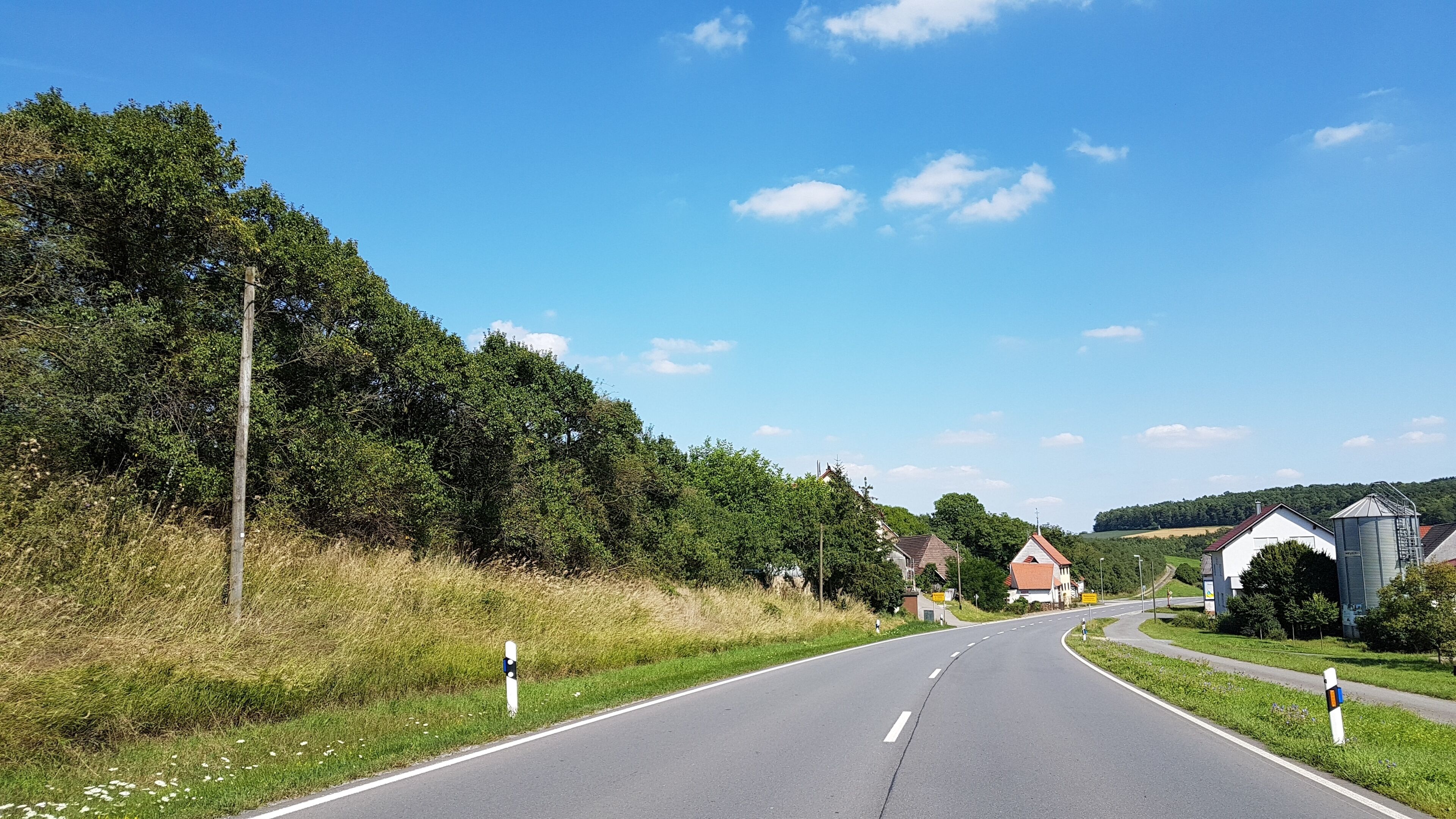 A rural road flanked by trees and houses.