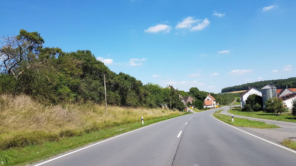 A rural road flanked by greenery and houses.