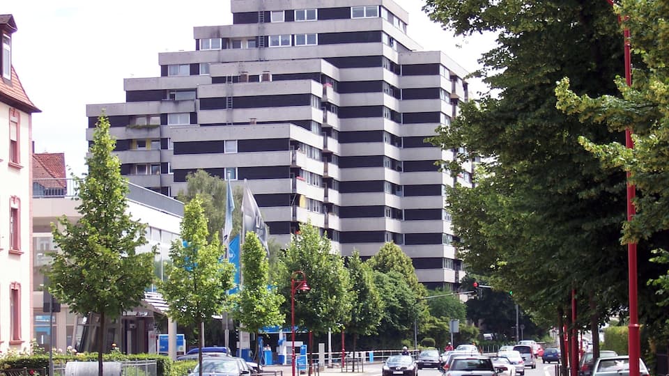 A multi-story building, a street lined with trees, and parked cars.
