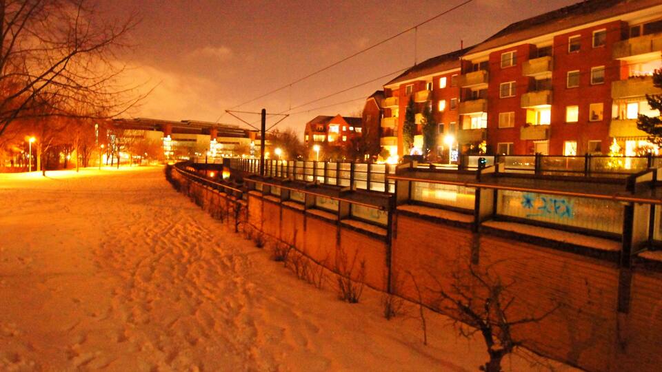 Lumipeitteinen polku, jonka vieressä on aita ja taustalla näkyy rakennuksia.