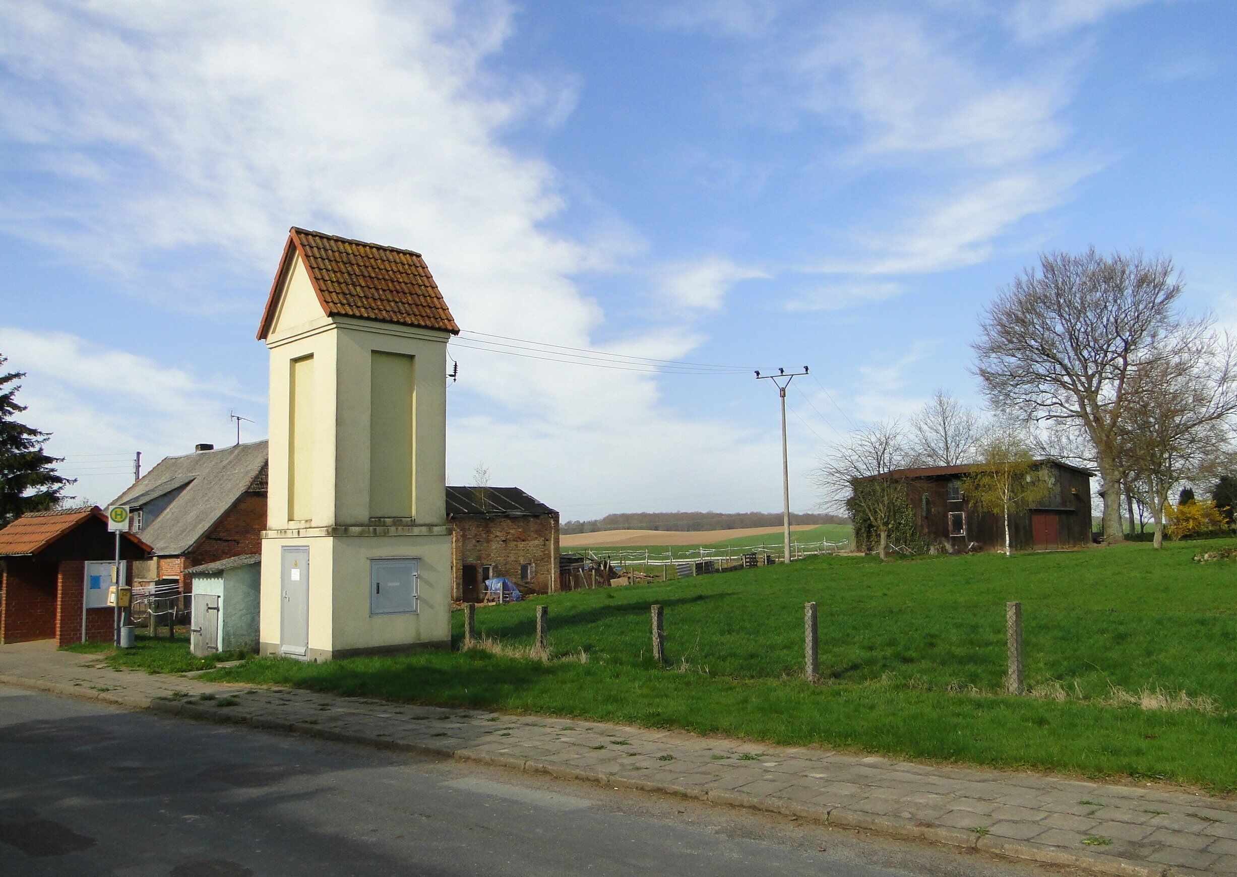 A rural landscape with a prominent white tower, a brick building, and a green field.