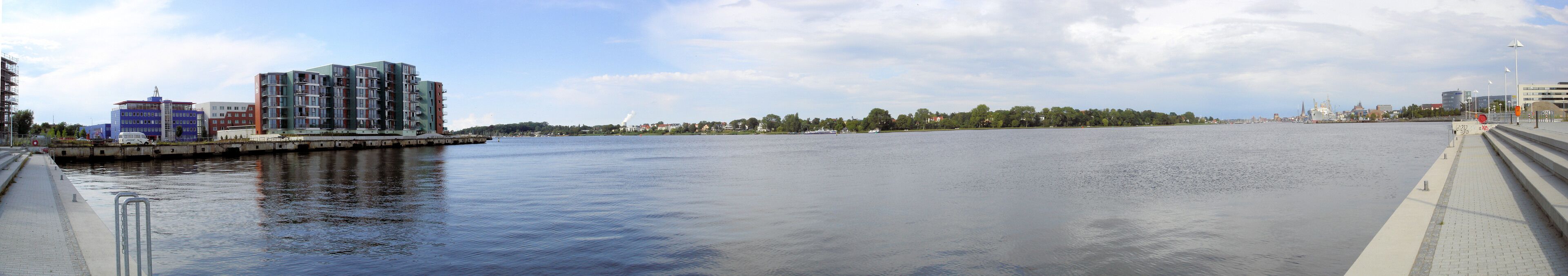 A river with a bridge, modern buildings, and a distant city skyline.