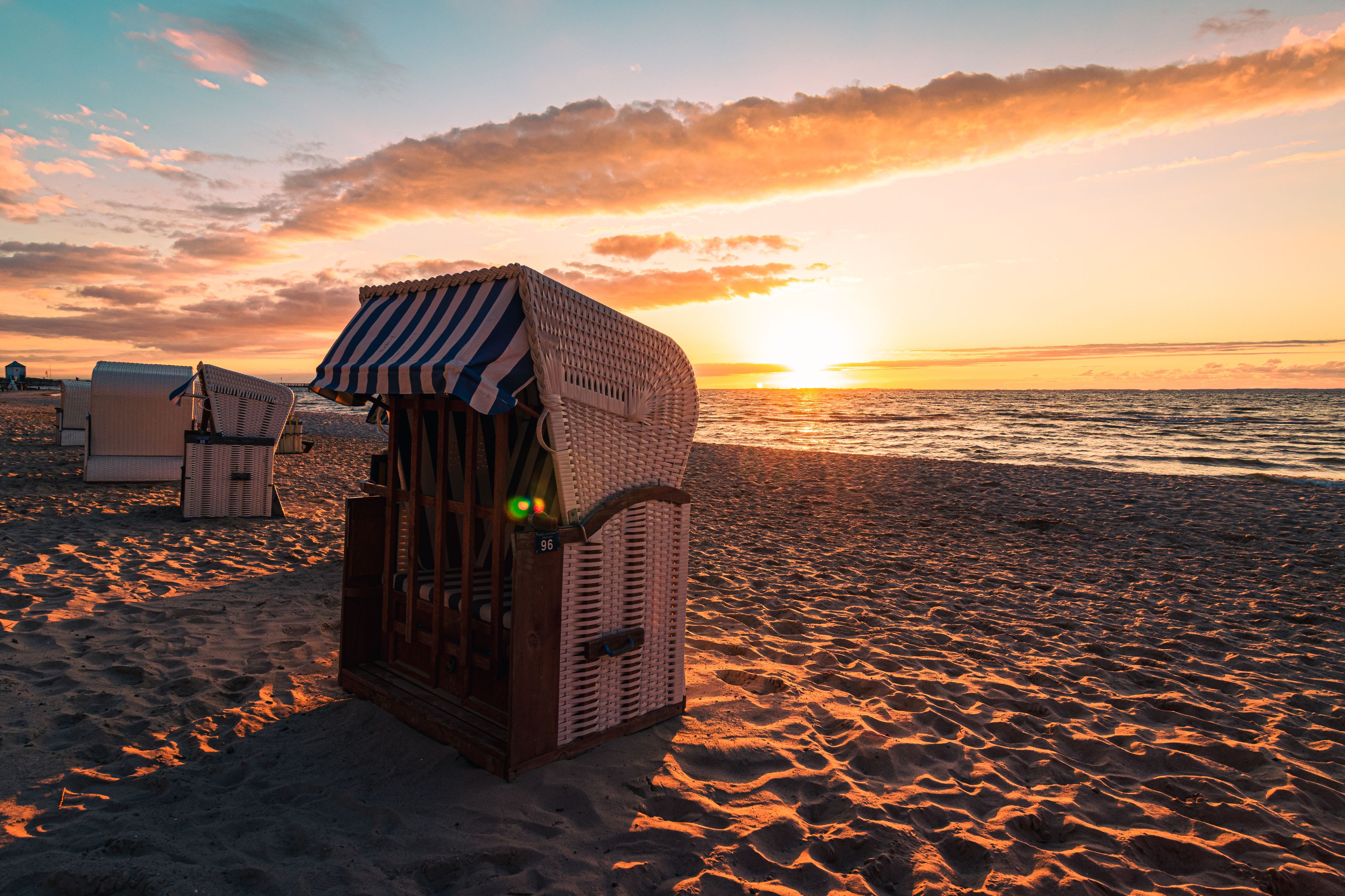 Une structure en bois située au bord de la plage, dotée d’un auvent rayé et entourée de sable et de chaises de plage.