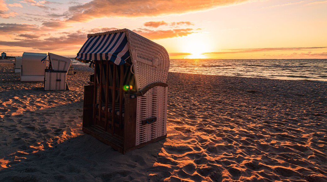 Une structure en bois située au bord de la plage, dotée d’un auvent rayé et entourée de sable et de chaises de plage.