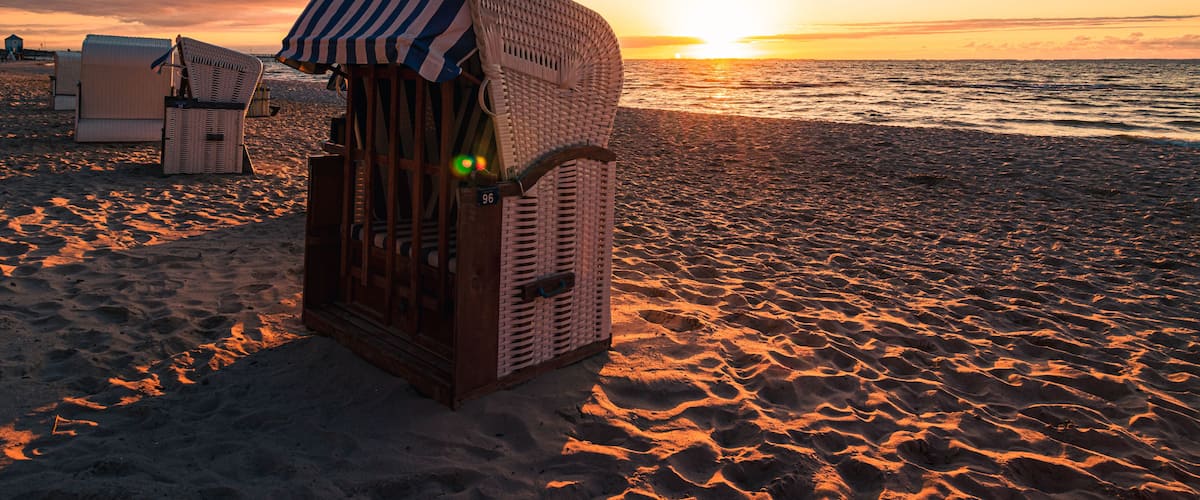 Una estructura de madera en la playa con toldo a rayas, rodeada de arena y sillas de playa.