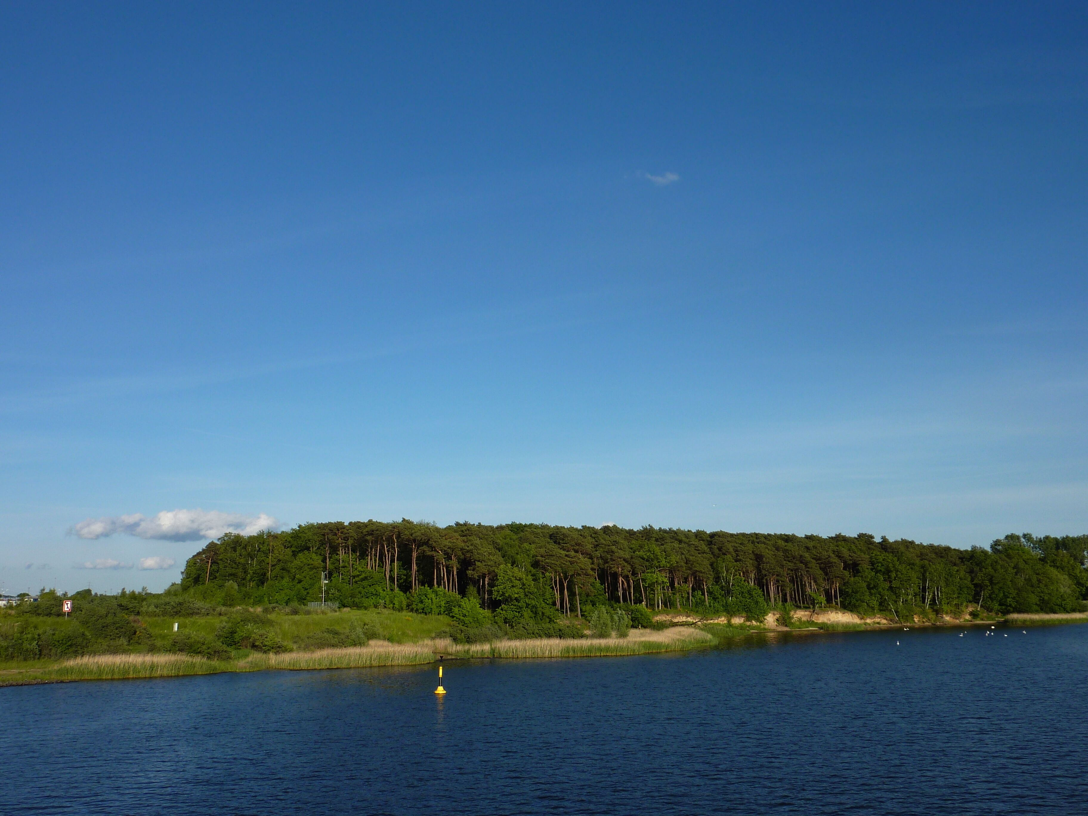 A lake with a forested shoreline and a buoy in the water.