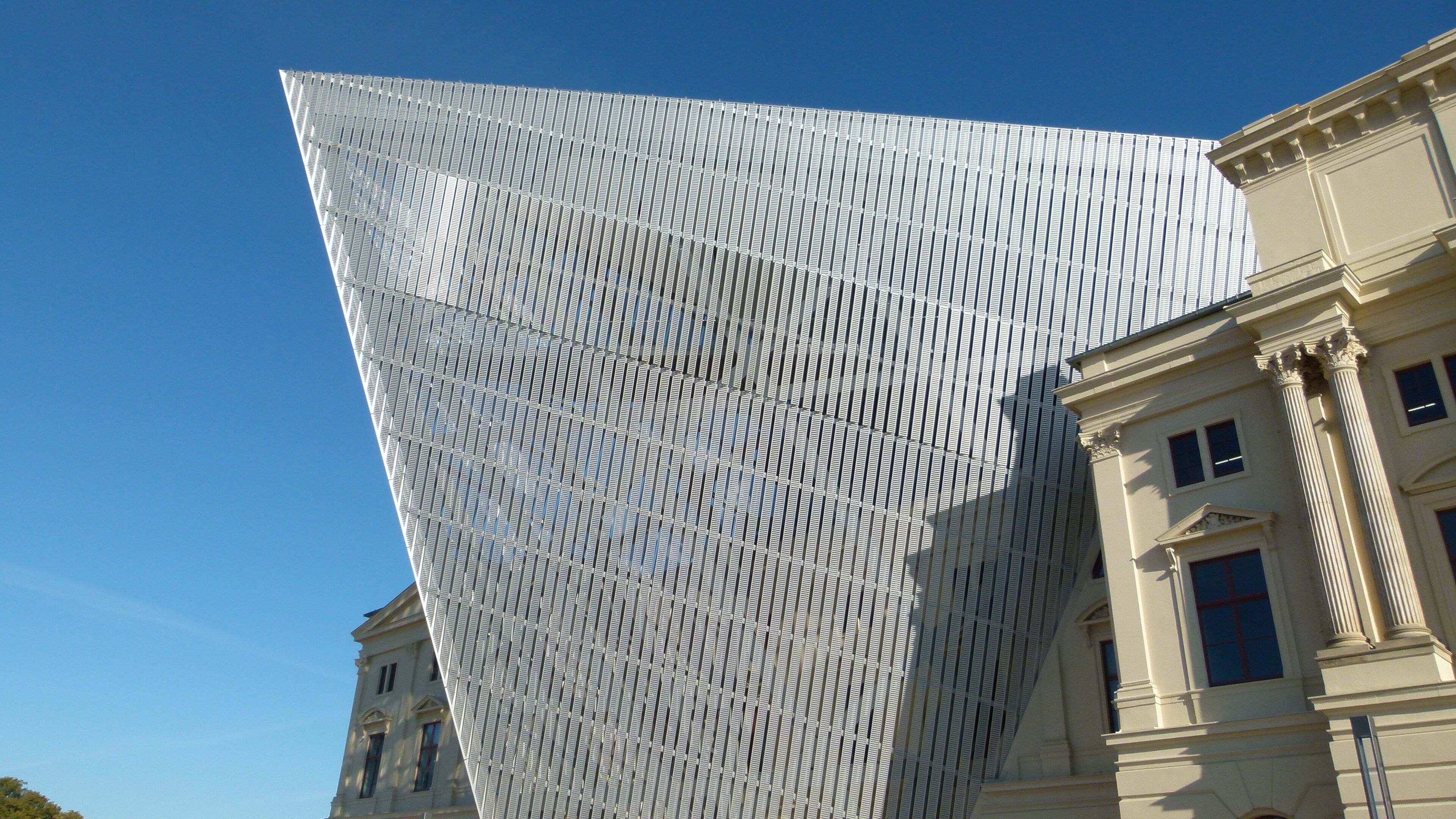 A modern building with a unique geometric facade and classical architecture nearby.