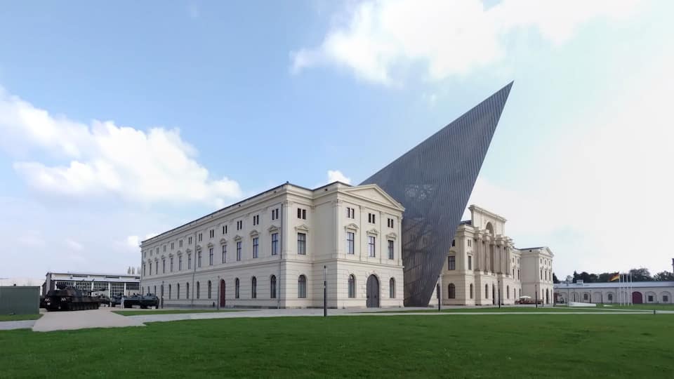 A large white building with arched windows and a modern glass structure.