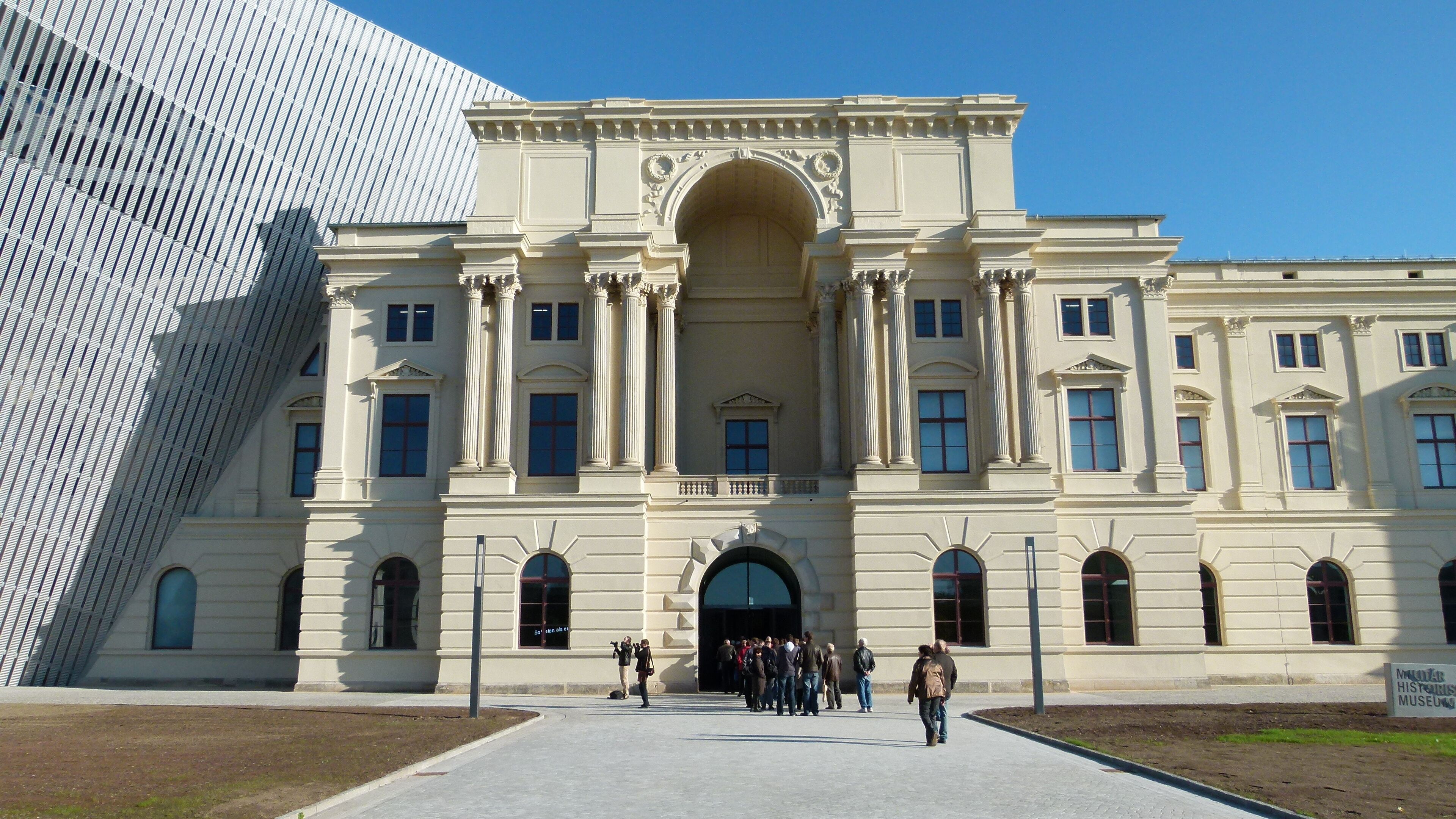 A historic building with classical architecture, including columns and arched windows, in front of a modern structure.