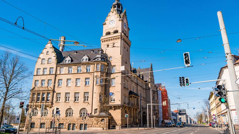 Ein historisches Gebäude mit einem Uhrturm, Straßenbahnschienen und blauem Himmel.