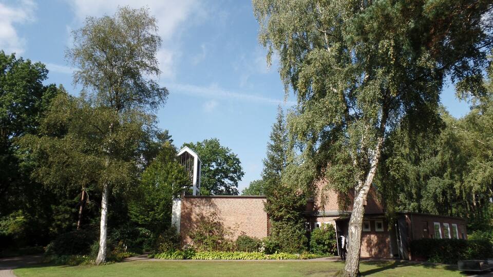 A park with a brick building, trees, and a clear sky.