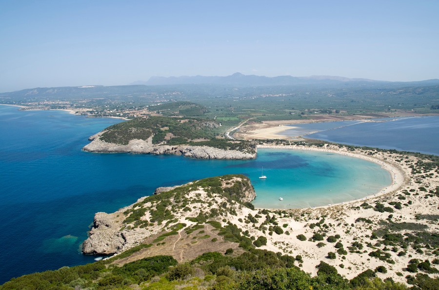 A coastal landscape with a bay, sandy beaches, rocky outcrops, and a clear blue sea.